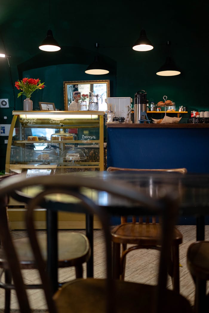 Warm café interior with wooden furniture, counter, and display case showcasing pastries.